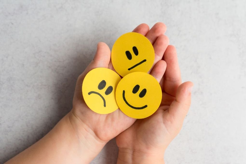 Child holding emoji faces showing happy, sad, and neutral emotions illustrating how to teach kids emotional intelligence