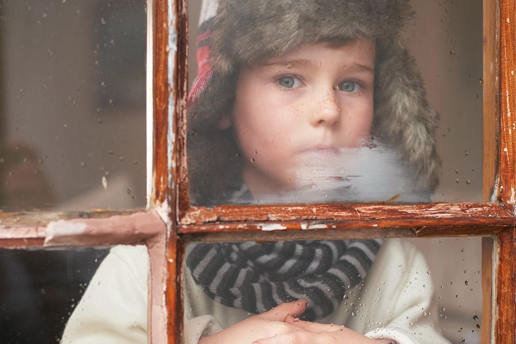 Child looking out of a window appearing sad, showing how kids can't tell you how they're feeling as they struggle to express emotions with words