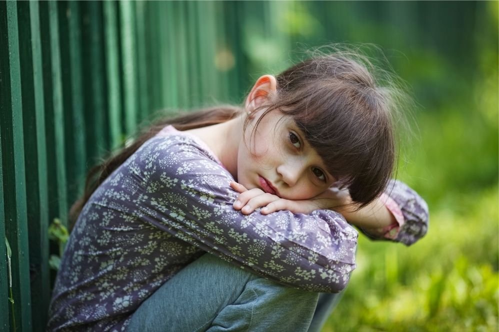 Understanding your child’s behavior: sad little girl sitting quietly by a garden fence