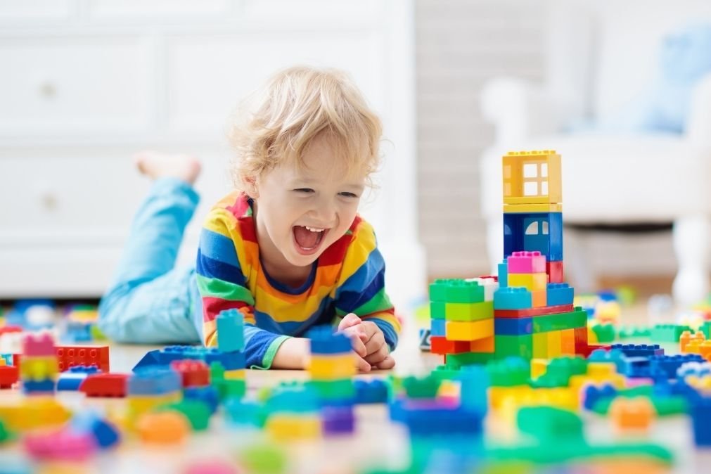Child laughing while building with colorful Lego bricks illustrating why play is important for children